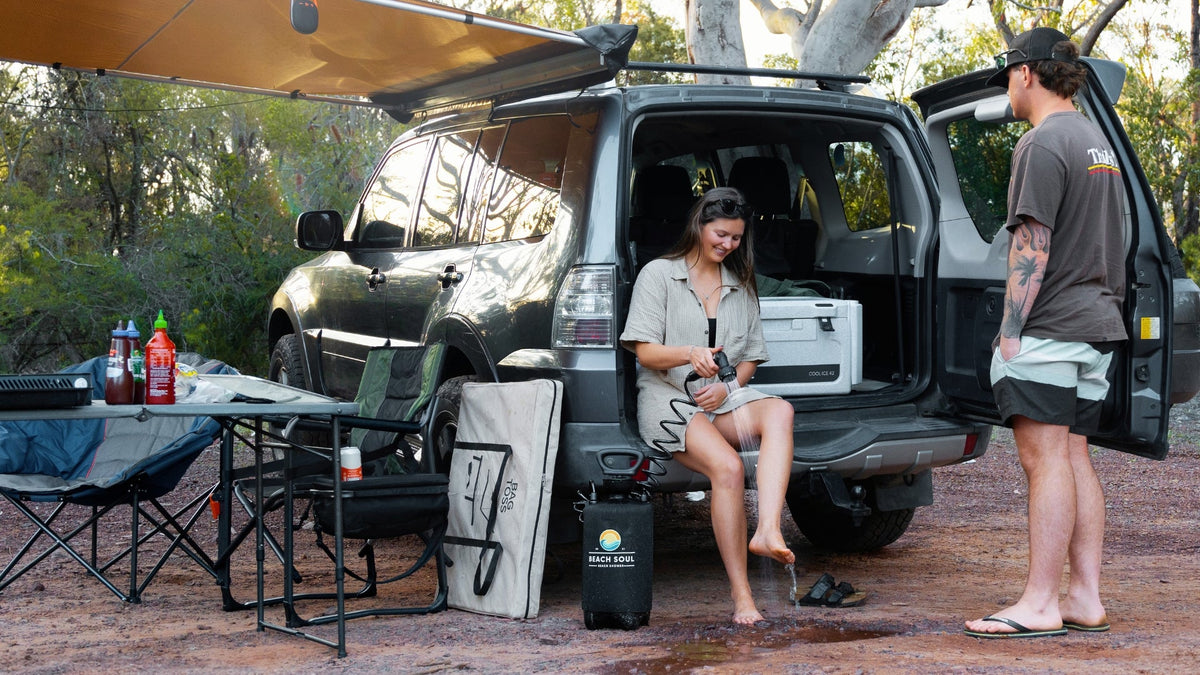 she seated on teh boot of the jeep Woman seated on the boot of a Jeep washing her feet with a Beach Soul portable shower at a campsite