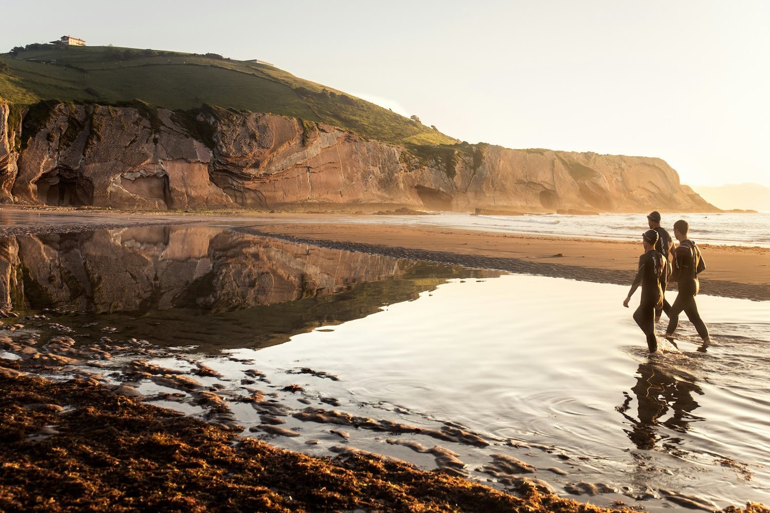 Surfers walking beside a coastal rock pool before entering cold water