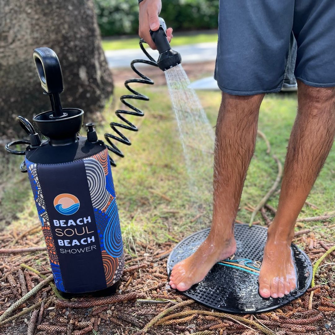 Man rinsing his feet with a Beach Soul portable shower while standing on the outdoor shower mat