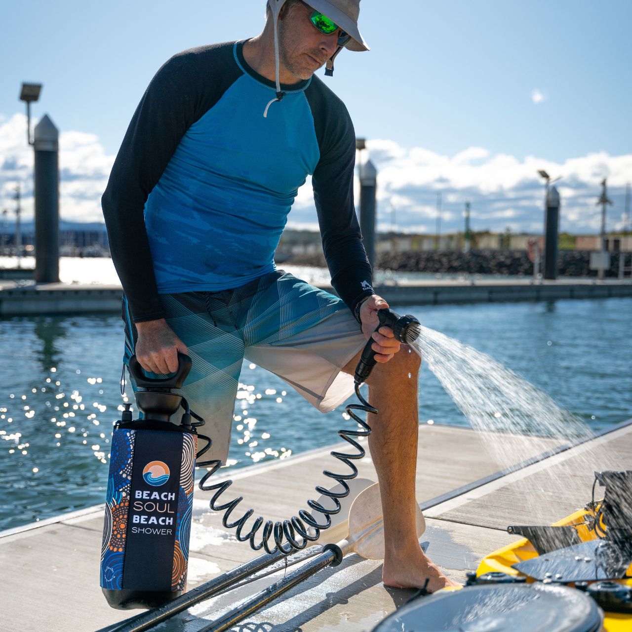 Man using the Jamigam portable shower to rinse his kayak beside the water