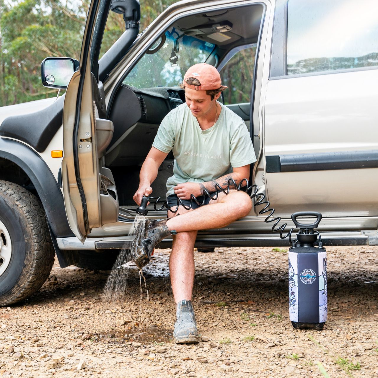 Man rinsing off with a Beach Soul Skully portable shower beside a vehicle