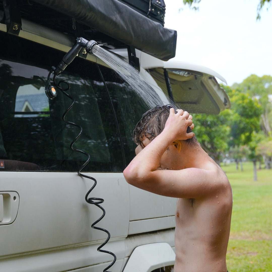Man rinsing his face under a Beach Soul shower head mounted to a vehicle with the Shower Holder