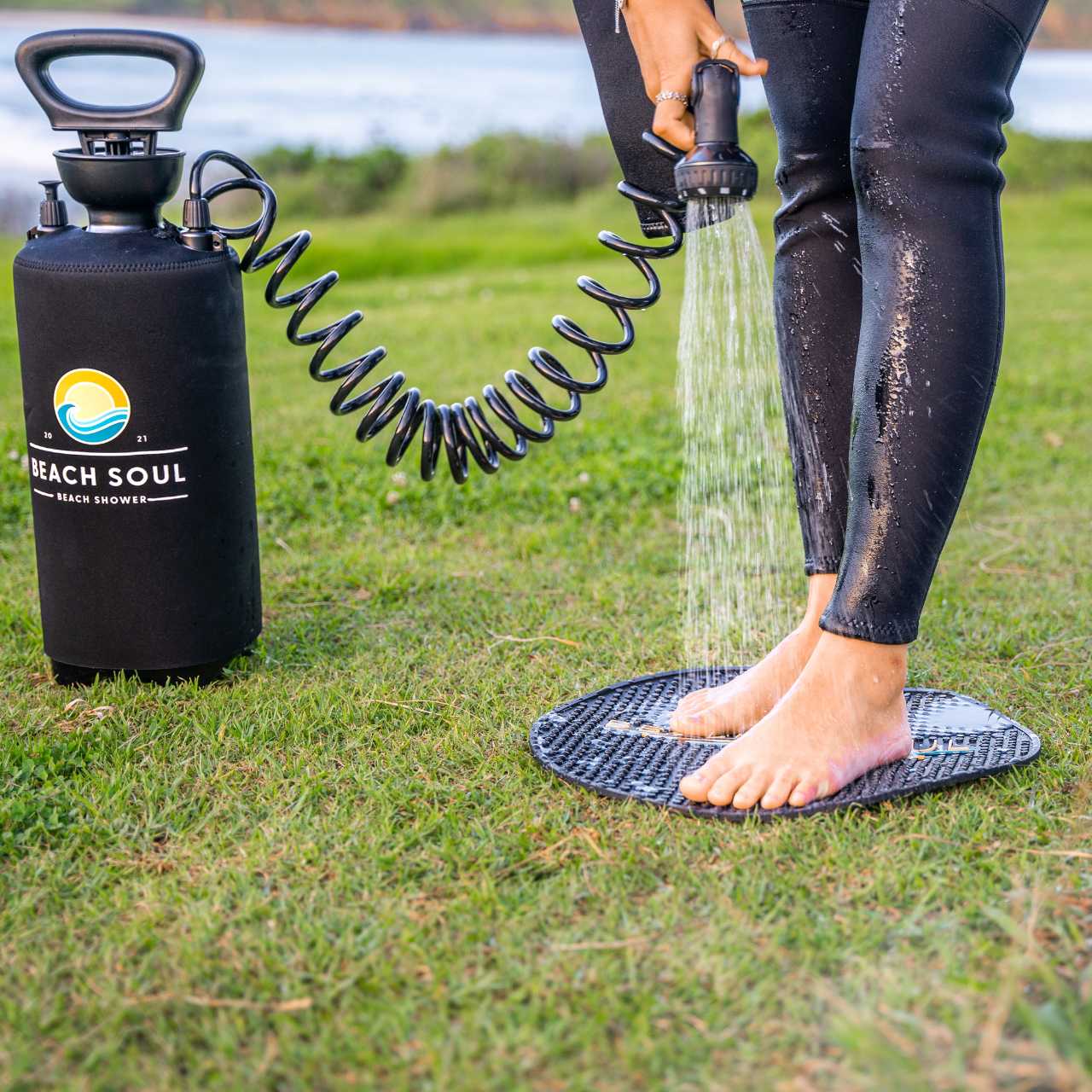 Person rinsing a foot with a Beach Soul portable shower while standing on the outdoor shower mat