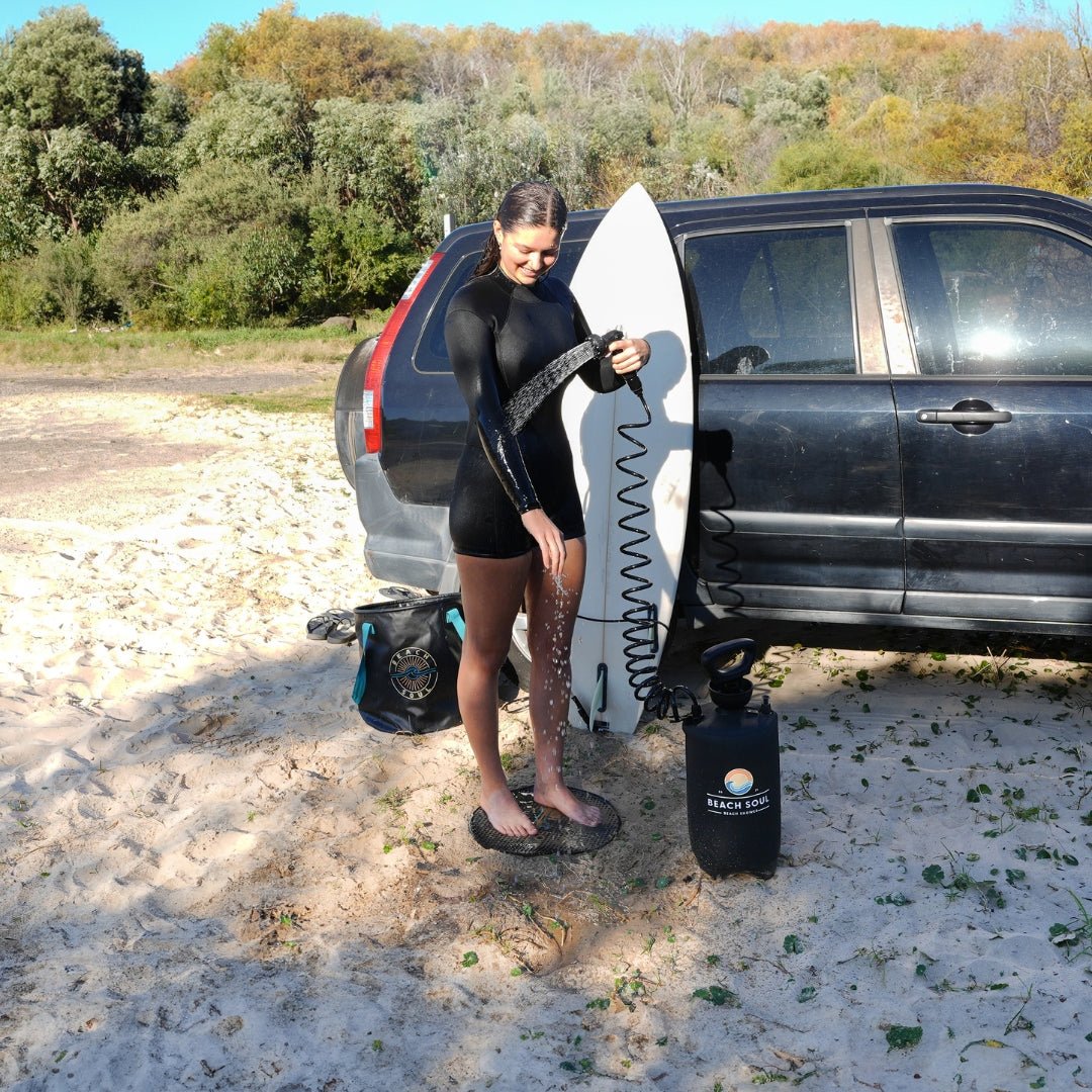 Surfer using the PRO portable shower to rinse off, with the Beach Shower Holder attached to the side window of the car