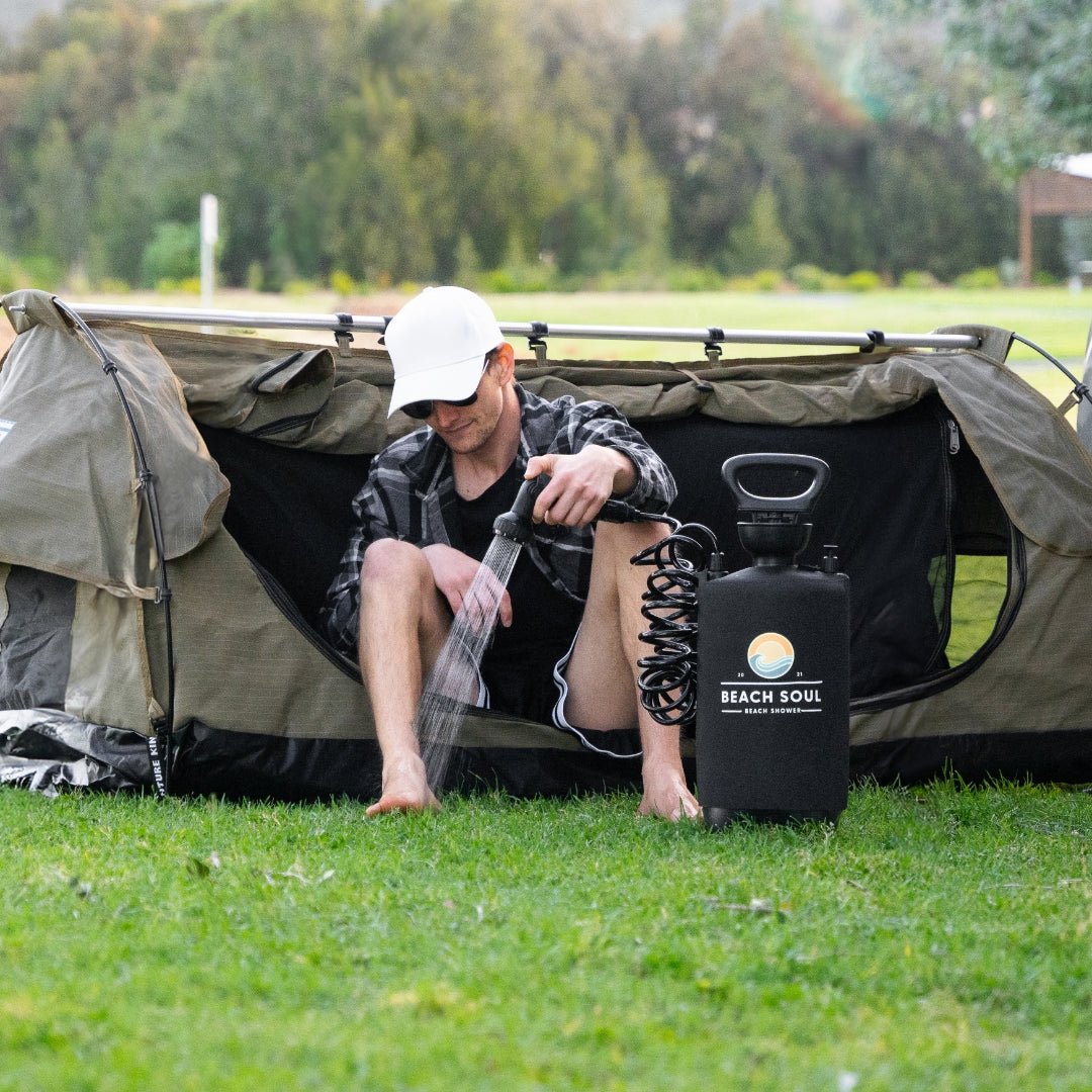 Man using the PRO portable shower to rinse his feet beside a camping tent