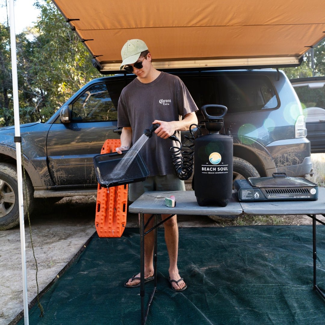 Man using the PRO portable shower to wash cookware beside his camp setup