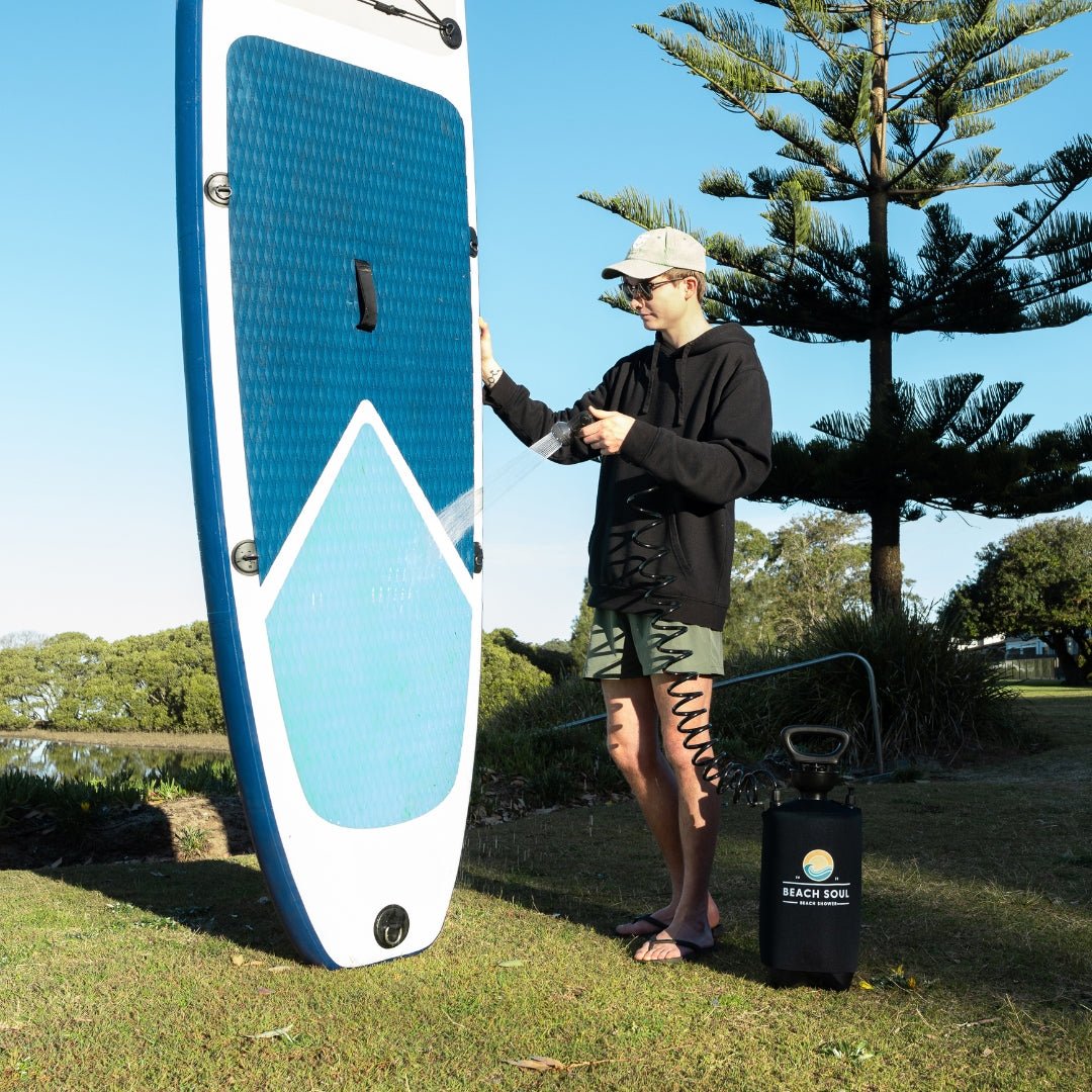 Man using the PRO portable shower to rinse a stand-up paddleboard outdoors