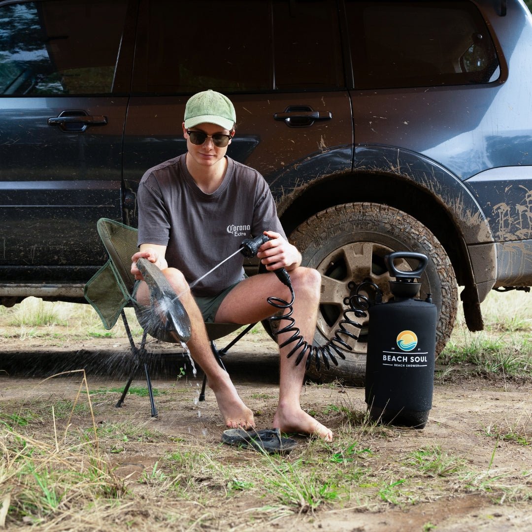 Man using the PRO portable shower while seated beside his campsite