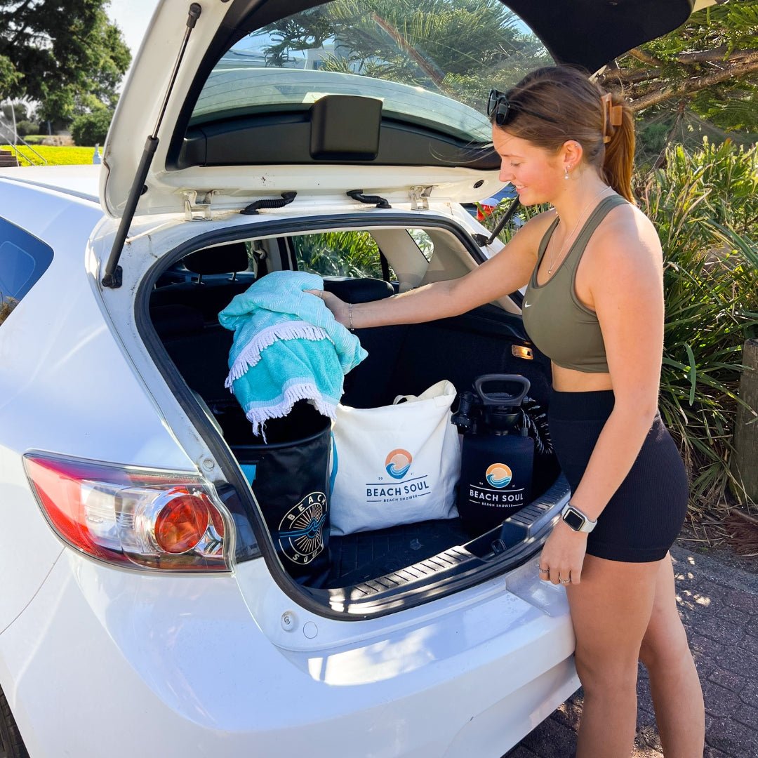 Woman packing towels and beach gear into the natural Beach Soul Beach Bag at an open car boot