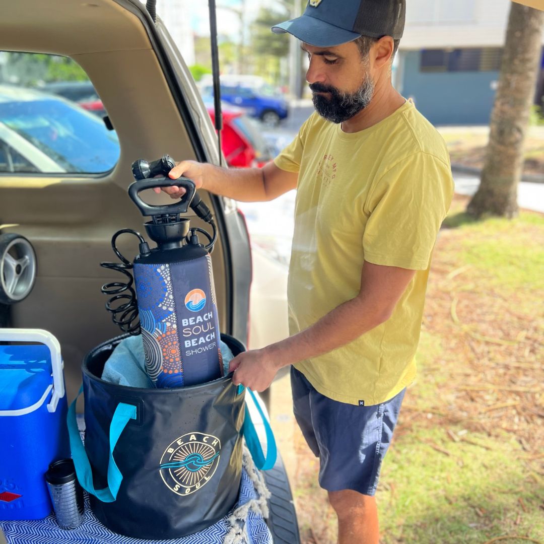 Man packing a Beach Soul portable shower into the Beach Soul Bag 'n' Mat beside a vehicle