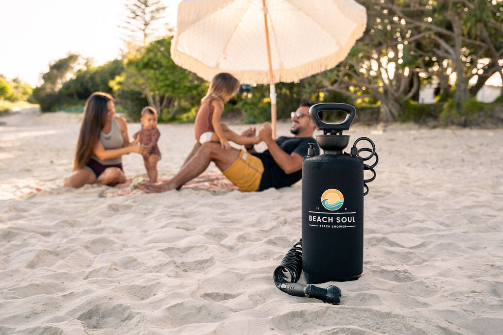 Family relaxing on the beach beside a Beach Soul portable shower in the sand