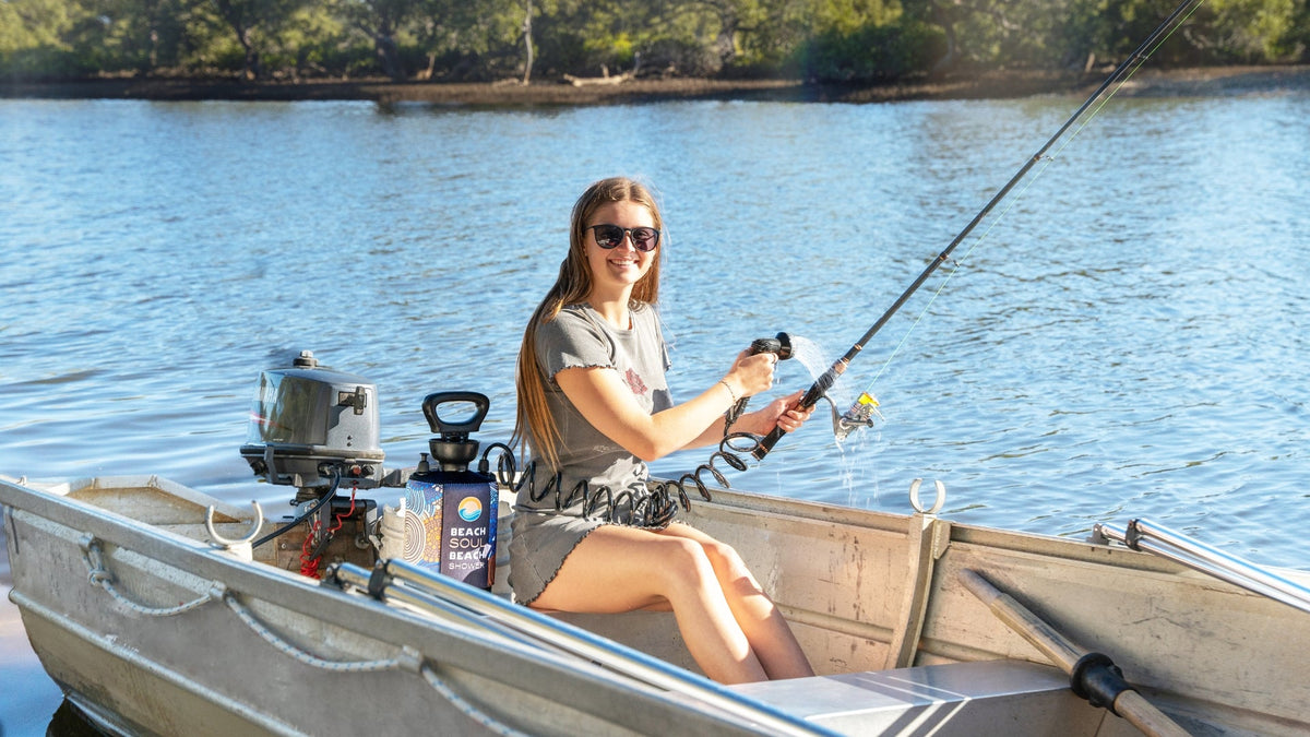 Woman rinsing a fishing rod and reel with a Beach Soul portable shower aboard a small fishing boat